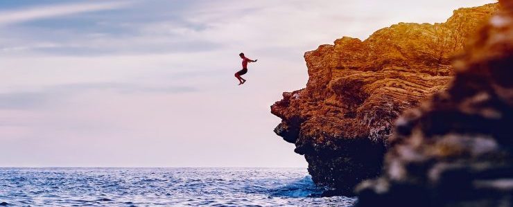 man jumping over cliff into water