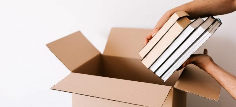 Man packing stack of books in opened cardboard box