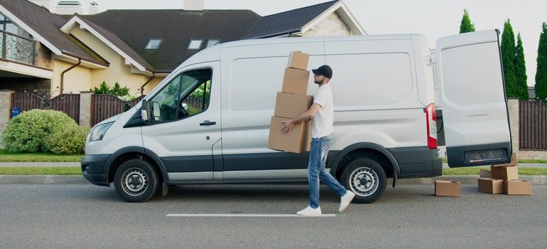 Man in white t-shirt and blue denim jeans carrying boxes from the white van