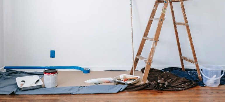 There is paint, cloth and brushes on the floor, and a bucket next to ladders.